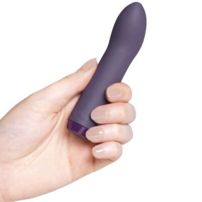 Vibrador roxo acinzentado com a ponta curva sendo segurada por uma mão feminina.