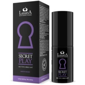 Imagem de um frasco de LuxuriA Secret Play, lubrificante para brinquedos sexuais. A embalagem é preta com detalhes em roxo e apresenta um ícone de fechadura estilizada. O produto é descrito como lubrificante de longa duração, à base de água e com fórmula não pegajosa, desenvolvido para melhorar a experiência com brinquedos íntimos. A embalagem também exibe o logotipo da LuxuriA, com o slogan 'Secret moments of passion', sugerindo uma experiência mais confortável e prazerosa.